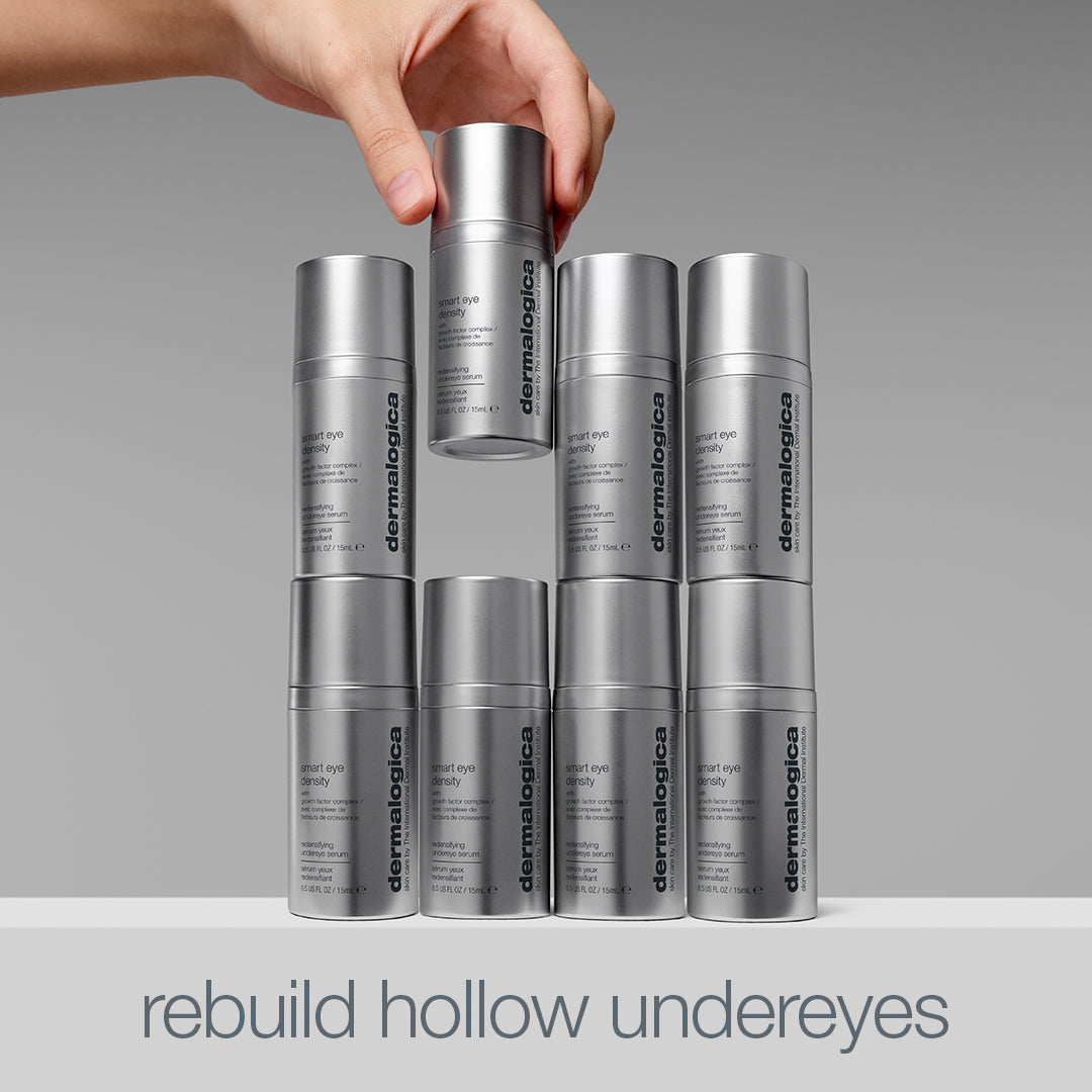 A hand places a silver Dermalogica South Africa smart eye density undereye serum bottle atop a stack of similar bottles, arranged to resemble two eyes. Text below reads: rebuild hollow undereyes and diminish dark circles.