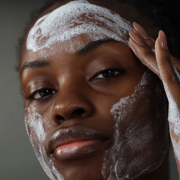 A person gently cleanses their forehead, cheeks, and chin with the foamy Dermalogica South Africa skin transformation duo, using one hand on their forehead, against a neutral background.
