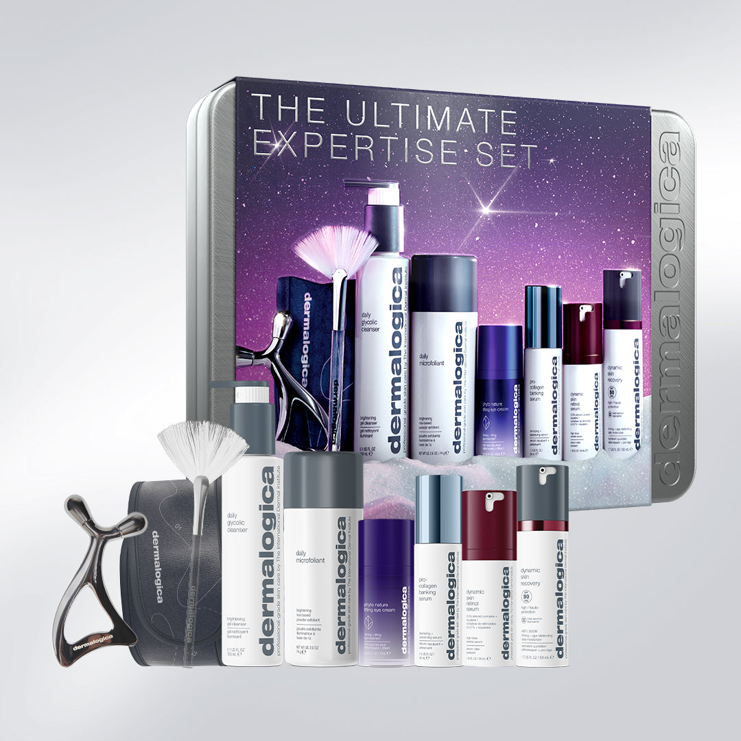 The ultimate expertise set includes a daily microfoliant, retinol serum, four full-size bottles, a metal facial massage tool, a fan-shaped brush, and a headband arranged in front of a starry purple and silver collectors tin.