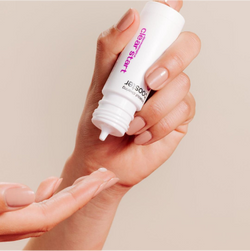 A hand squeezes a white tube of skincare product labeled clear start onto the fingers of the other hand against a neutral background.