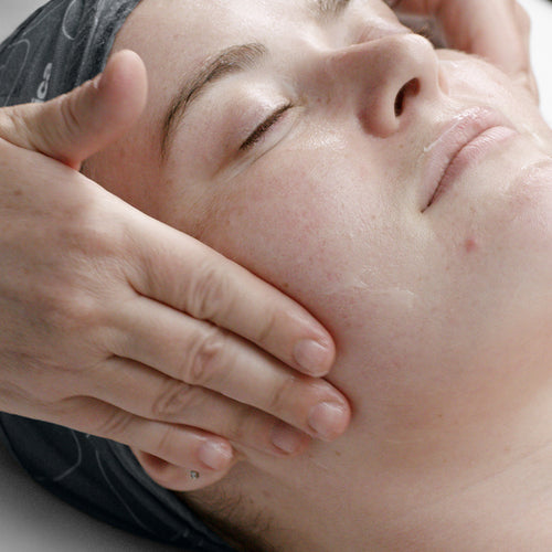 A person with closed eyes receives a gentle facial massage while wearing a headband. Their clean, breakout-prone skin appears slightly moisturized after using Dermalogica pro clear treatment.