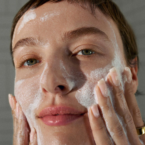 A close-up of a person using Dermalogica daily microfoliant, massaging the foamy cleanser onto their cheeks with both hands for dewy, radiant skin.