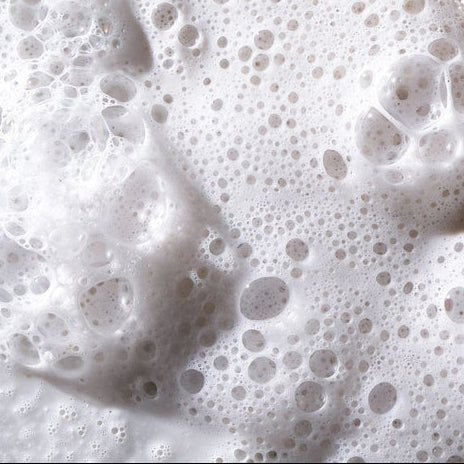 Close-up of foamy liquid spreading over Dermalogica daily microfoliant, creating a circular indentation in the white exfoliating powder—a dynamic reveal of its skin brightening action.