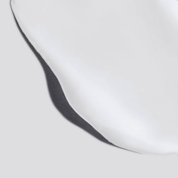 A close-up of Dermalogica body hydrating cream—a glossy, white formula with smooth edges enriched with lactic acid—spreading across a light gray surface.