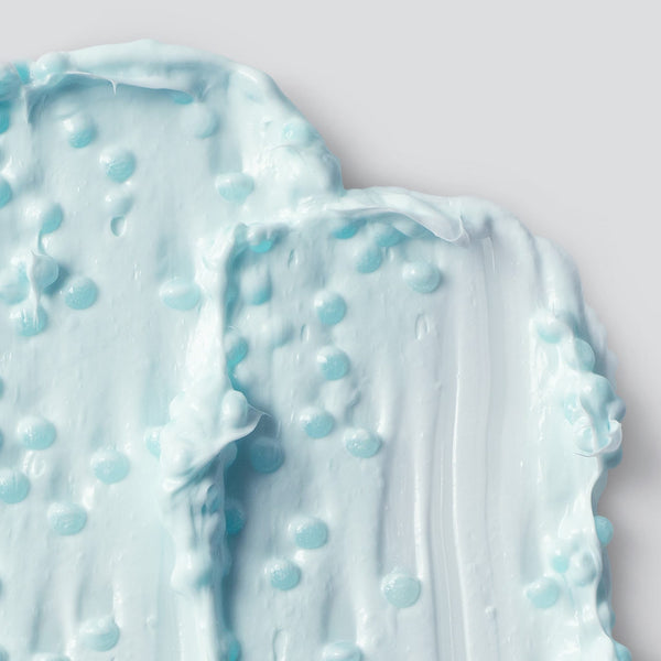Dermalogica hydro masque exfoliant is a light blue, creamy hydrating mask with small blue beads and exfoliating bamboo, shown in thick smooth layers on a pale gray background. The texture appears glossy and rich.