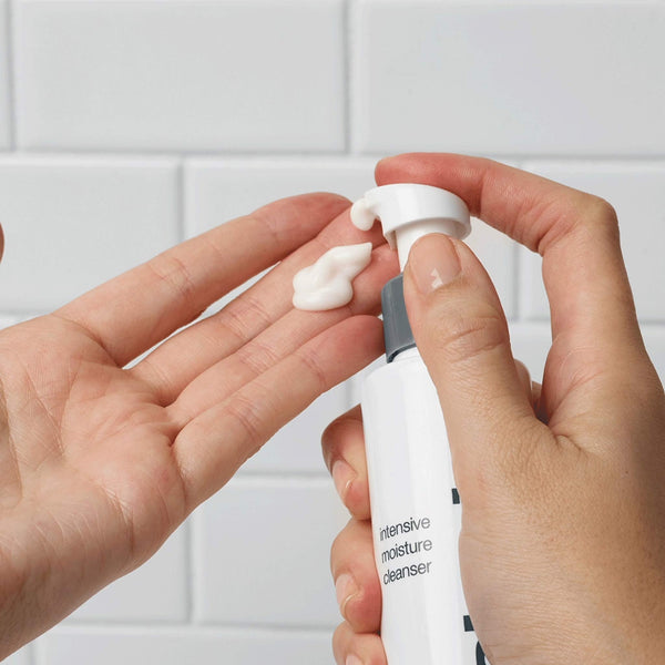 A person dispenses Dermalogica intensive moisture cleanser, ideal for dry skin, onto their fingertips with a white tiled wall in the background.