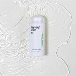 A bottle of Clear Start foaming wash is placed on a white surface, surrounded by a splash of clear liquid, creating a fresh and clean look.