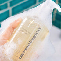 A clear pump bottle of Dermalogica conditioning body wash with a silver dispenser holds light yellow liquid. The label features essential oils such as eucalyptus and lavender, offering a nourishing cleanse for the skin.
