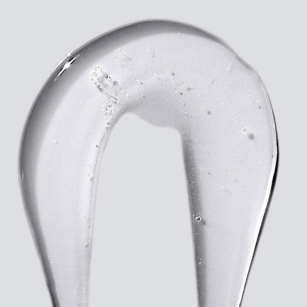 A close-up of Dermalogica’s conditioning body wash gel spread in a curved line on a light grey background, revealing small bubbles within its clear, skin-nourishing formula.