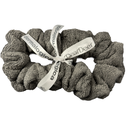 A soft, textured gray headband from the gift | anti-drip wrist wash band set by Dermalogica South Africa is rolled up and tied with a white ribbon featuring brand logos—perfect for skincare or spa routines.