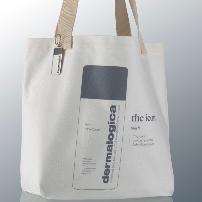 A white tote bag with tan handles features a large graphic of a Dermalogica Daily Microfoliant bottle and the text the icon. and The iconic powder exfoliant Daily Microfoliant.