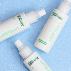 Three white bottles of Dermalogica Clear Start Micro-Pore Mist are arranged on a light blue surface with water droplets, suggesting a fresh and hydrating skincare product.