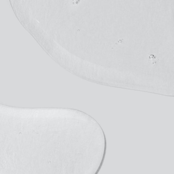 Clear gel-like liquid with small air bubbles, spread in two irregular shapes on a smooth, light gray background—Dermalogica’s skin hydrating booster is infused with Hyaluronic Acid to help maintain lasting moisture balance.